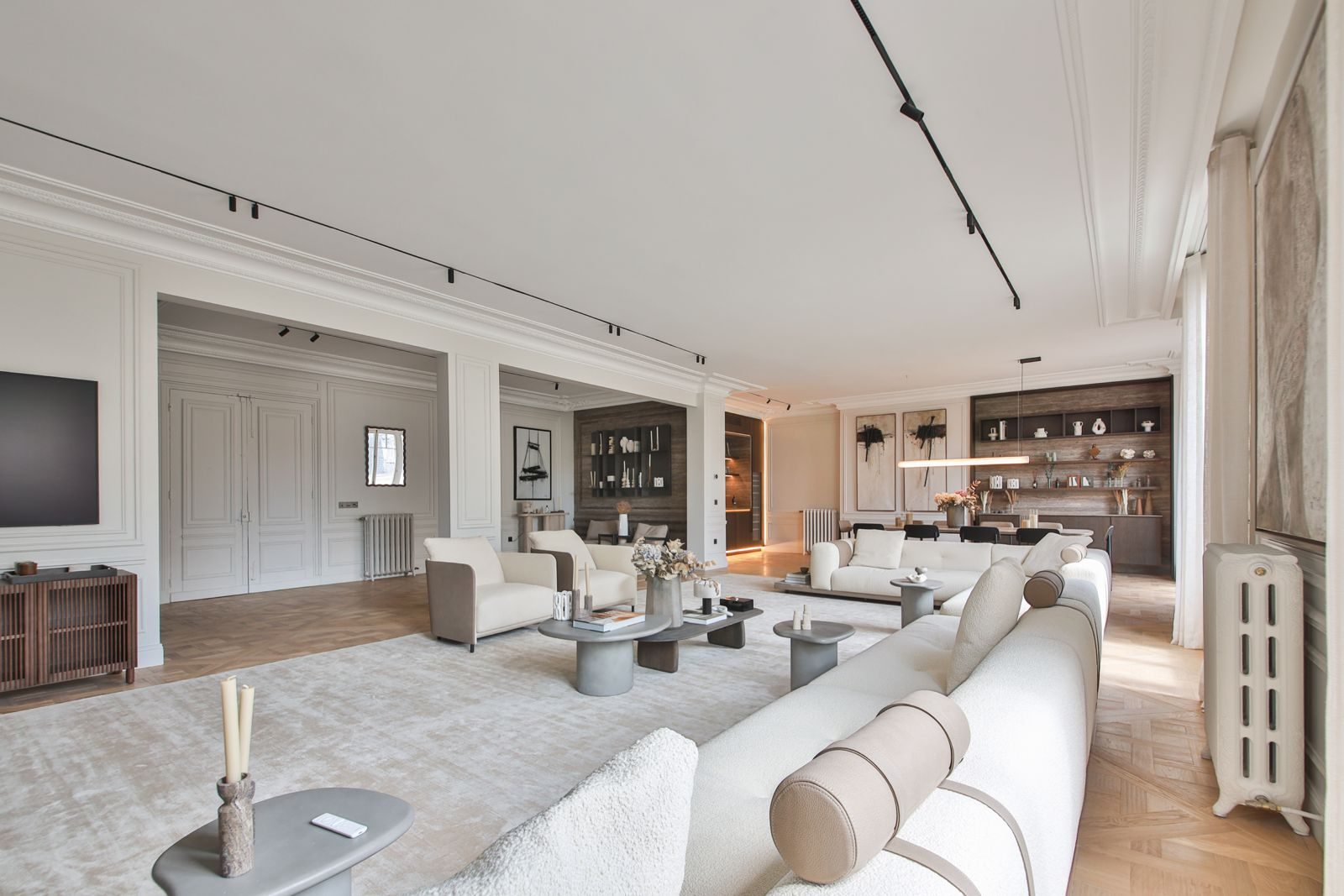 Large salon of a renovated Haussmann apartment in Paris, with sofas, panelled walls and a dining area