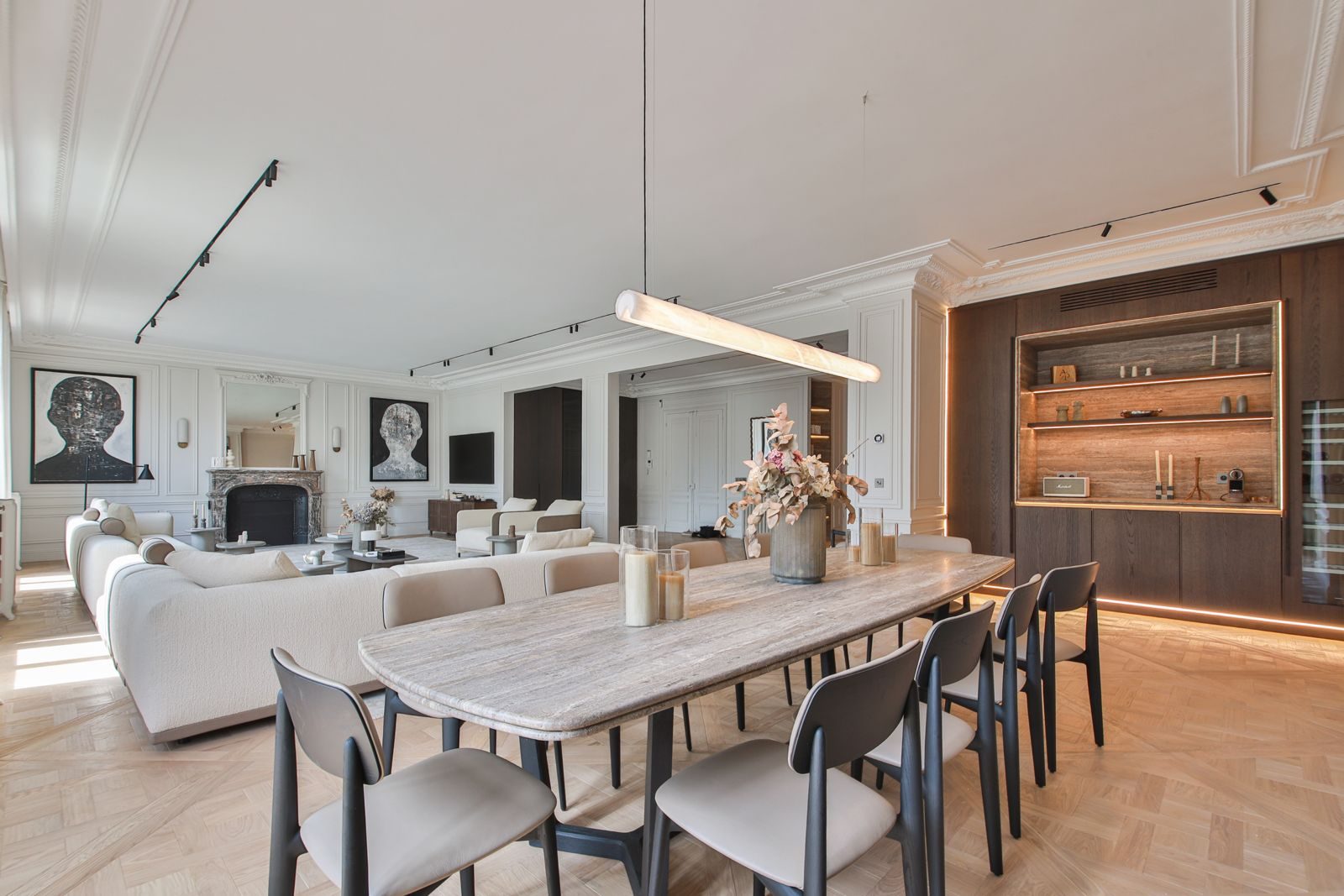 Dining room opening onto the salon of a Paris apartment, travertine table and lit oak shelving